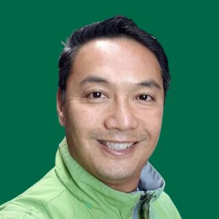 Happy man with short, dark hair in a light green jacket stands smiling against a solid green background, radiating positive energy.