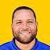 Smiling bearded man with short hair in a blue shirt stands against a vibrant yellow background, ideal for featured front page images.