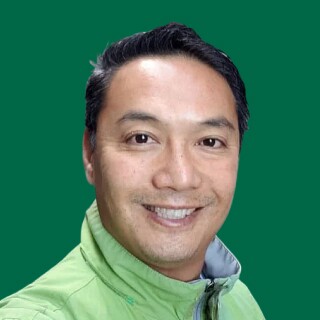 Happy man with short, dark hair in a light green jacket stands smiling against a solid green background, radiating positive energy.