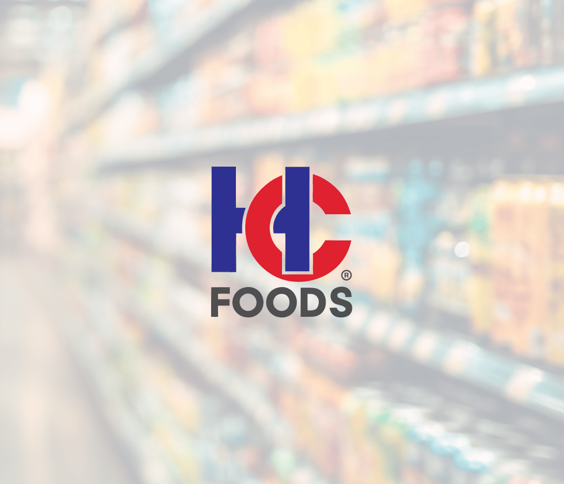Centered against a blurred grocery store aisle, the HC Foods logo stands out in blue and red amid shelves of assorted products.